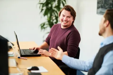 man achter laptop in geanimeerd gesprek met een collega