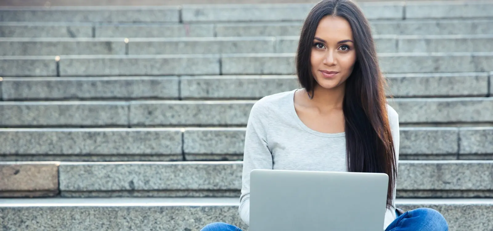 vrouw achter laptop kijkt lachend in de camera